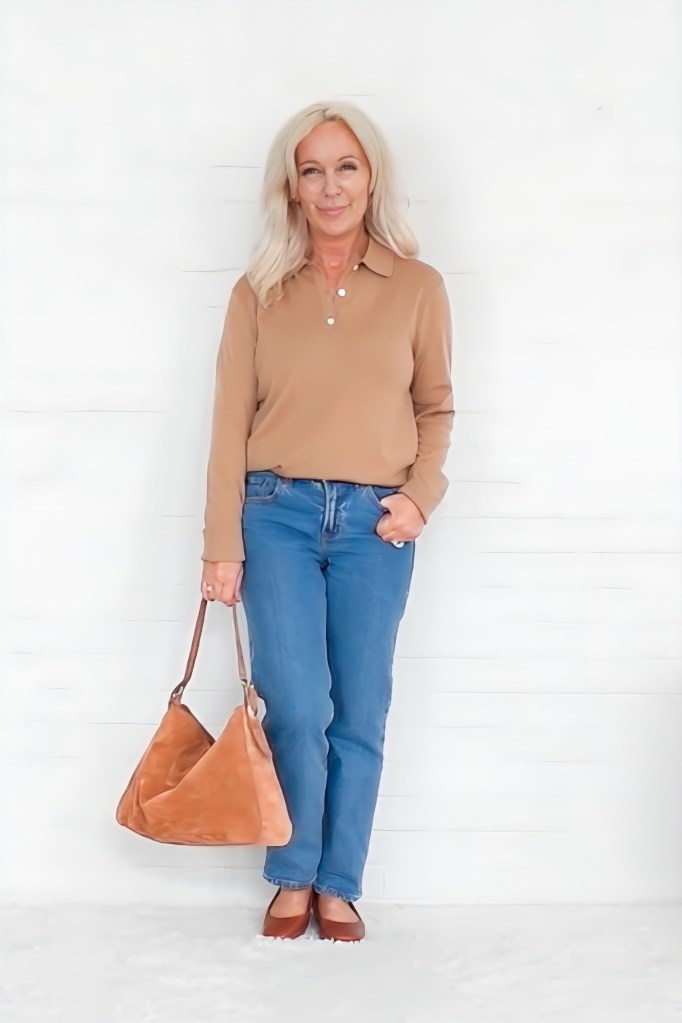 A woman with long blonde hair stands against a white background, wearing a tan polo shirt and blue jeans, holding a brown handbag.