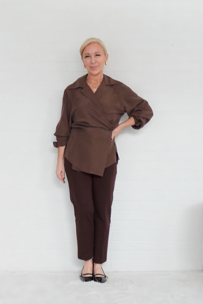 A woman wearing a brown wrap top and matching brown trousers stands confidently against a white background, showcasing a chic and polished outfit.