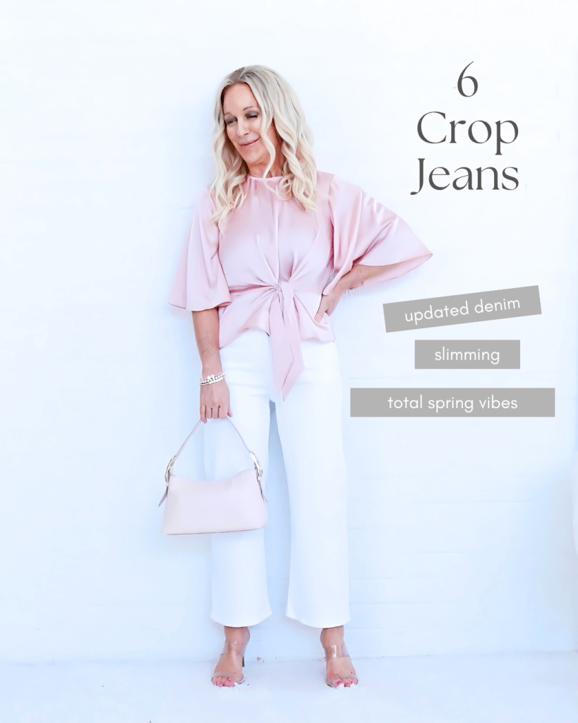 A woman wearing a pink blouse tied at the waist, standing in white crop jeans against a white background, holding a pink handbag.