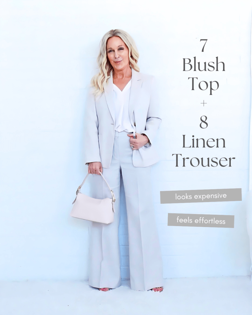 A woman wearing a stylish light grey blazer and matching linen trousers, holding a light bag, standing against a white background.