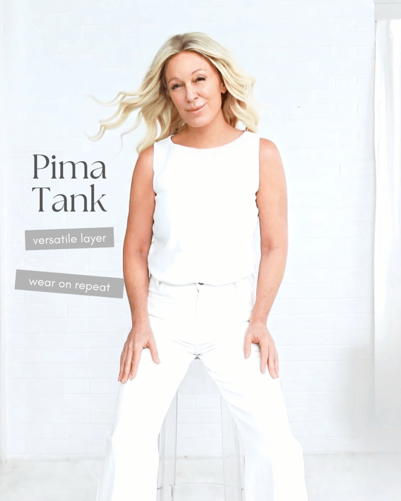 A woman wearing a white Pima tank top and white pants, sitting on a clear chair against a light-colored background, promoting a versatile layering piece.