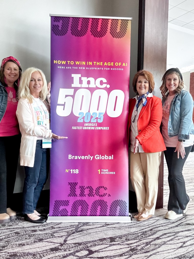Four women standing next to a colorful banner for Inc. 5000 2025, celebrating Bravenly Global as number 118 among America's fastest-growing companies.